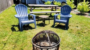 Un patio trasero con dos sillas Adirondack azules, una mesa de picnic de madera y un brasero.