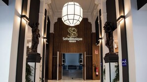 Fachada de un hotel de diseño moderno, que incluye una gran lámpara de araña, un mostrador de recepción y estatuas a cada lado de la entrada.