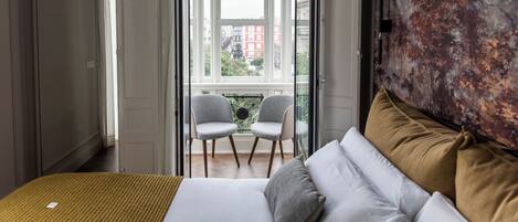 Une chambre à coucher avec un lit, deux chaises, une grande fenêtre et un tableau accroché au mur.