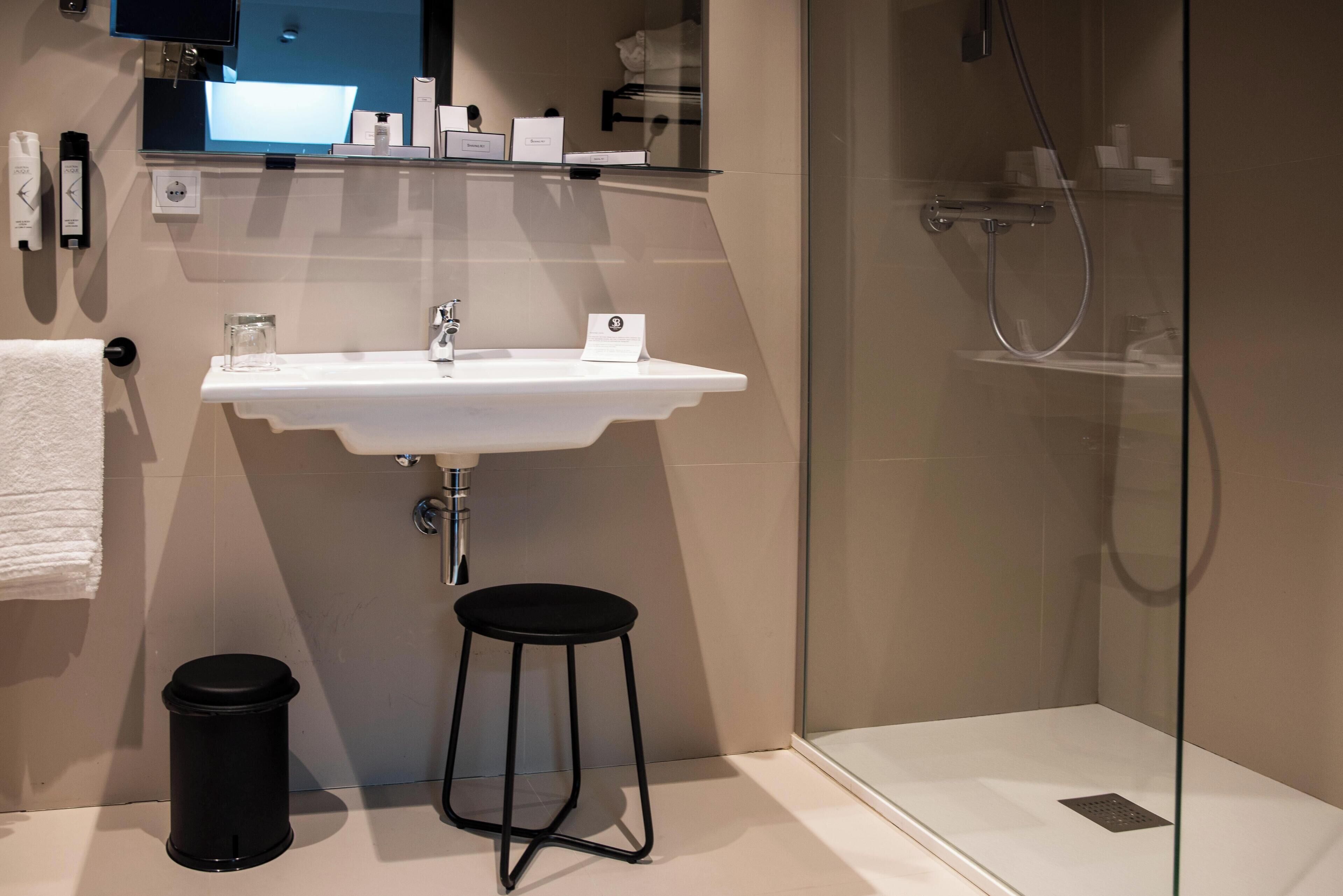 Un baño moderno con un lavamanos blanco, una cabina de ducha de vidrio y un cubo de basura negro.