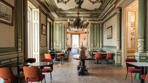 Un salón imponente con columnas decorativas, una araña y una mesa central.