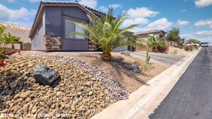 Um imóvel residencial com fachada em estuque, base de pedra e um jardim ajardinado com pedras e uma palmeira.