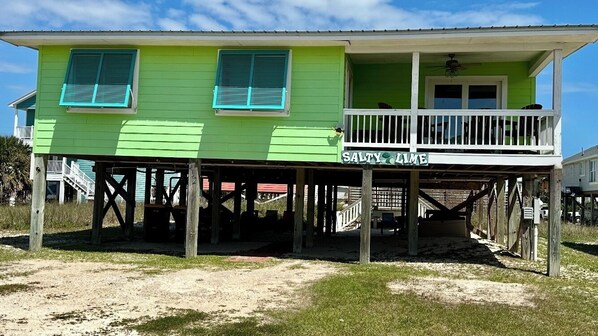 A green house with a balcony, a name sign reading 'SALTY AIR,' and a wooden deck structure. - Salty Lime, Pet Friendly! Beach House!  Sleeps 8 Steps from the beach! (Gulf Shores)
