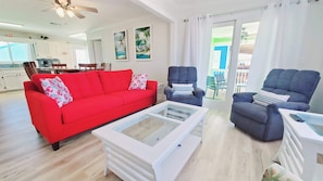 Relax in this inviting living room with a sofa, armchair, and coffee table, opening to a balcony with outdoor seating.
