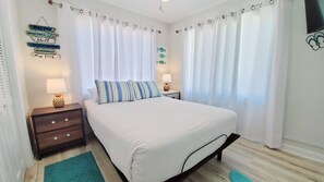 A neatly arranged bedroom with a bed, two bedside tables, a lamp, and a wall-mounted sign. - Salty Lime, Pet Friendly! Beach House!  Sleeps 8 Steps from the beach! (Gulf Shores)