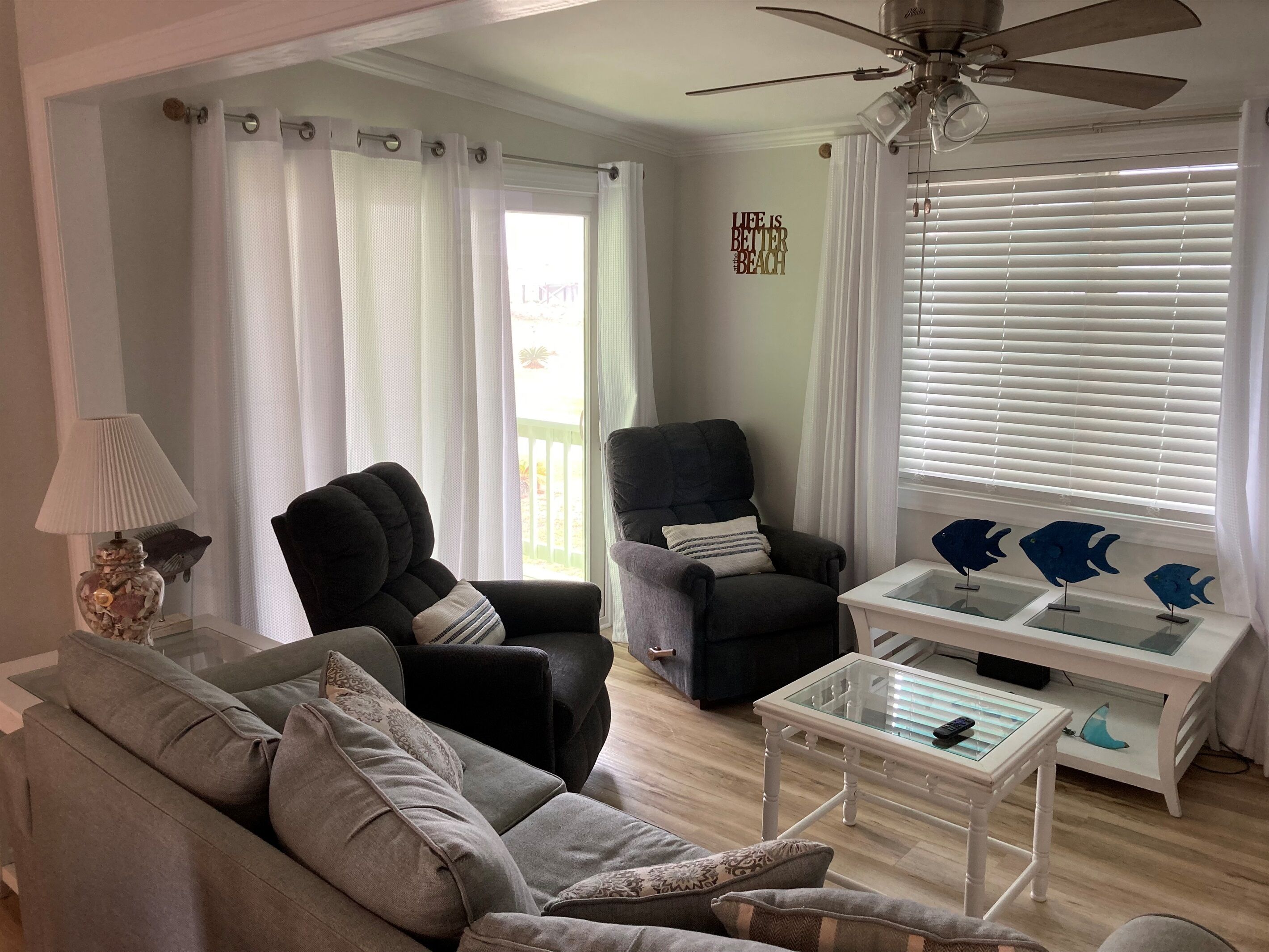 Un salon avec un canapé gris, deux fauteuils, une table basse et un ventilateur de plafond.