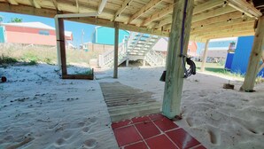A covered outdoor area with a wooden deck, a red tile entrance, and a staircase leading to a higher level. - Salty Lime, Pet Friendly! Beach House!  Sleeps 8 Steps from the beach! (Gulf Shores)