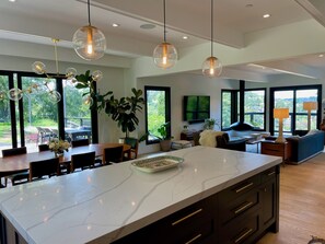 A modern kitchen with a large island, pendant lighting, and large windows offering views of the outdoors. - New Family Friendly Home in Mill Valley (MILL VALLEY)