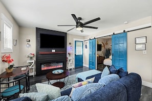 A living room with a fireplace, a ceiling fan, and a blue door leading to another room. - The Wespanee Wave - The Perfect Couples Getaway (Charleston)