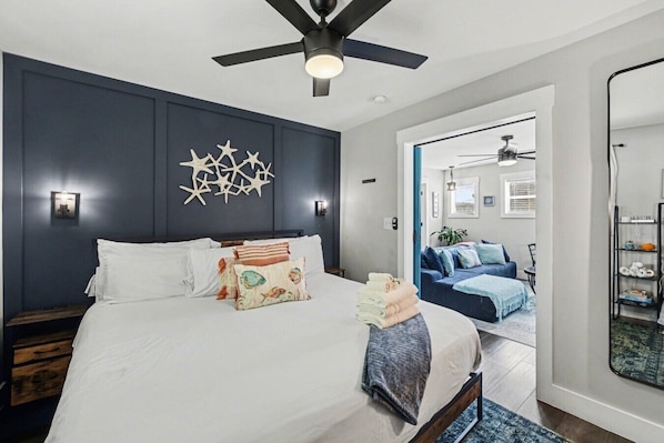 A bedroom with a bed, a ceiling fan, a wall-mounted star decoration, and a doorway leading to another room. - The Wespanee Wave - The Perfect Couples Getaway (Charleston)