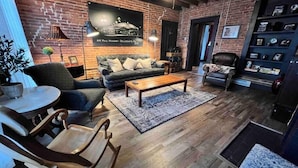 A cozy living room with a brick wall, a sofa, a coffee table, and a bookshelf. - Historic, Stylish Getaway 2 blocks from Waterfront (Bellefonte)