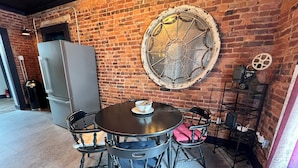 A dining area with a brick wall, a round table with chairs, a vintage mirror, and a refrigerator. - Historic, Stylish Getaway 2 blocks from Waterfront (Bellefonte)