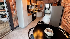 A compact kitchen with a dining area, featuring a brick wall, modern appliances, and a cozy seating arrangement. - Historic, Stylish Getaway 2 blocks from Waterfront (Bellefonte)