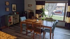 A dining area with a wooden table and chairs, a cabinet with decorative items, and a window with curtains. - Sturgis Rally rental; great location; next to I-90 and Harley Davidson (Rapid City)