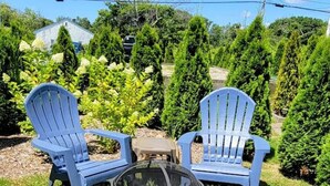 Two blue Adirondack chairs and a black fire pit in a grassy outdoor area with trees and a house in the background. - 2 BR beach condo, 1 block from shore! (Narragansett)