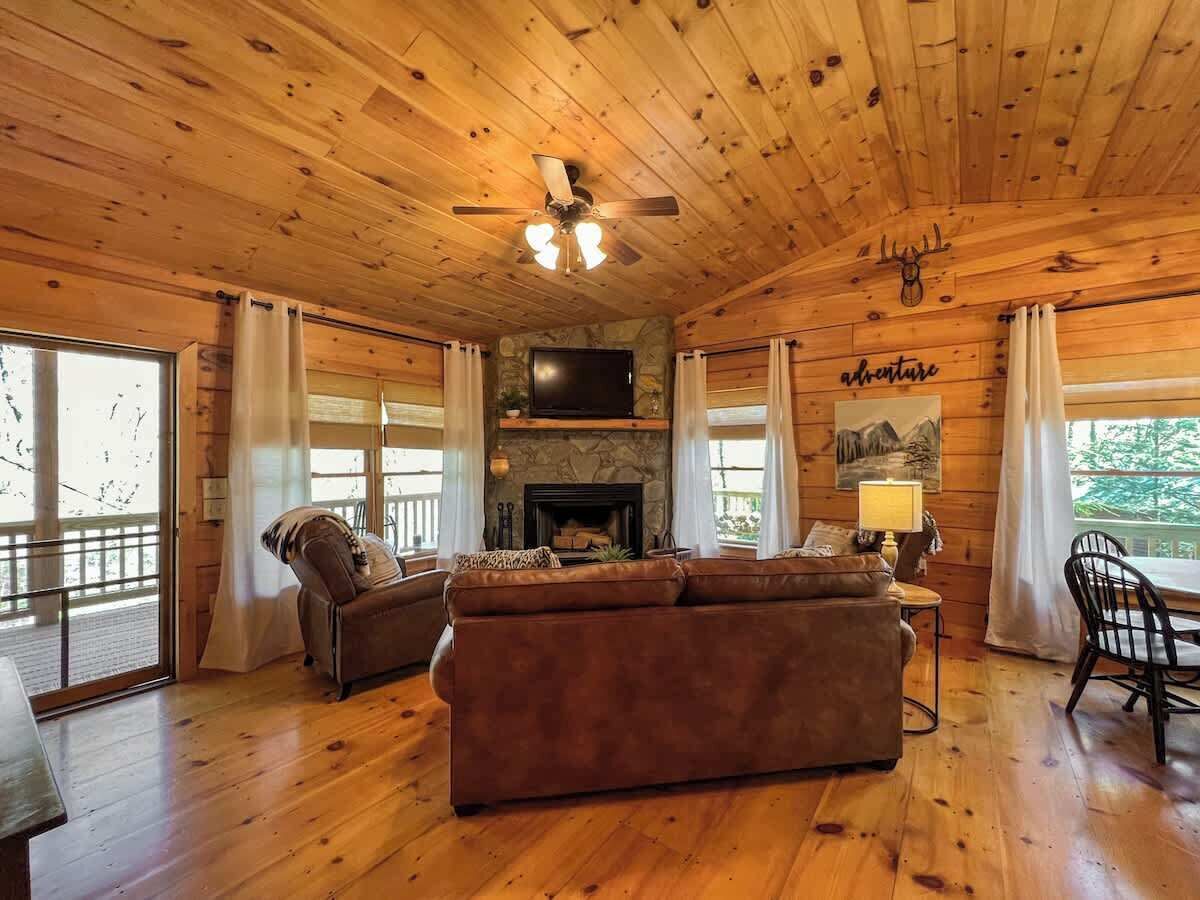 L’intérieur d’un chalet en bois, avec une cheminée, un canapé en cuir et un coin repas.