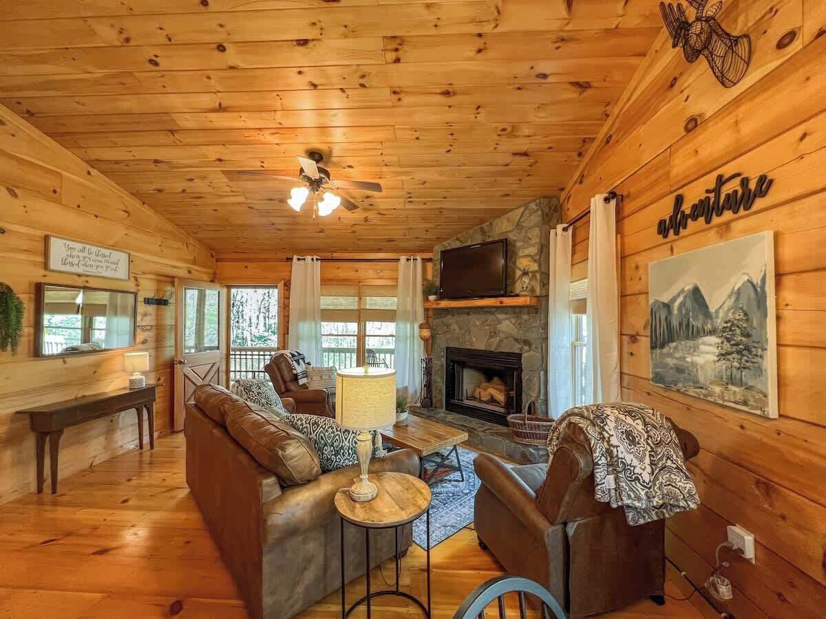 L’intérieur chaleureux d’un chalet avec un plafond en bois, une cheminée, un canapé, un téléviseur et un tableau accroché au mur.