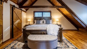 Een slaapkamer met een loft-achtige plafond, een bed met witte dekbedovertrek, twee bedlampen en een groot raam met jaloezieën.