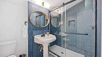 A bathroom with a pedestal sink, two round mirrors, a glass shower enclosure, and blue patterned tiles.