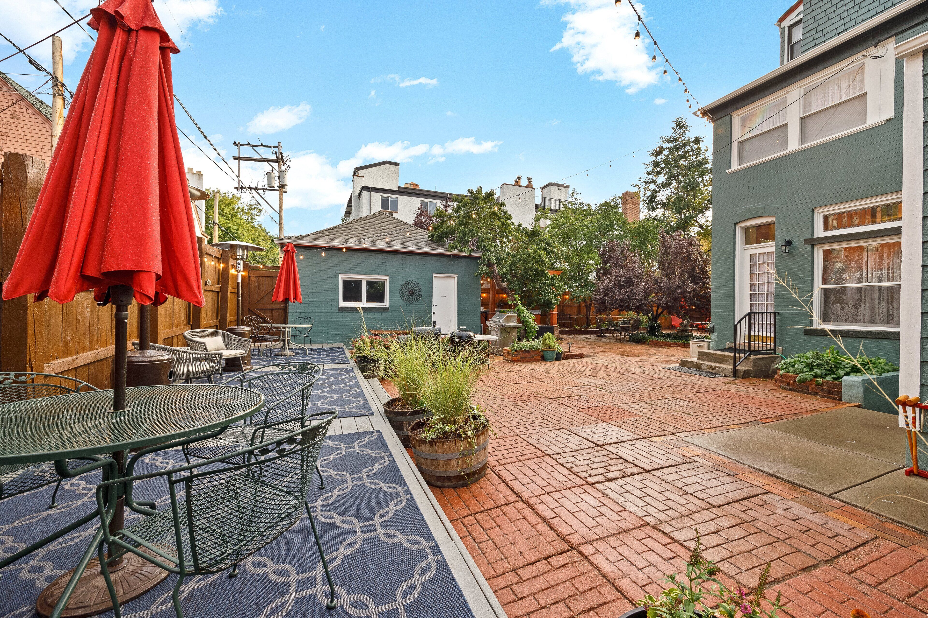 A patio area with tables and chairs, a red umbrella, and potted plants.
