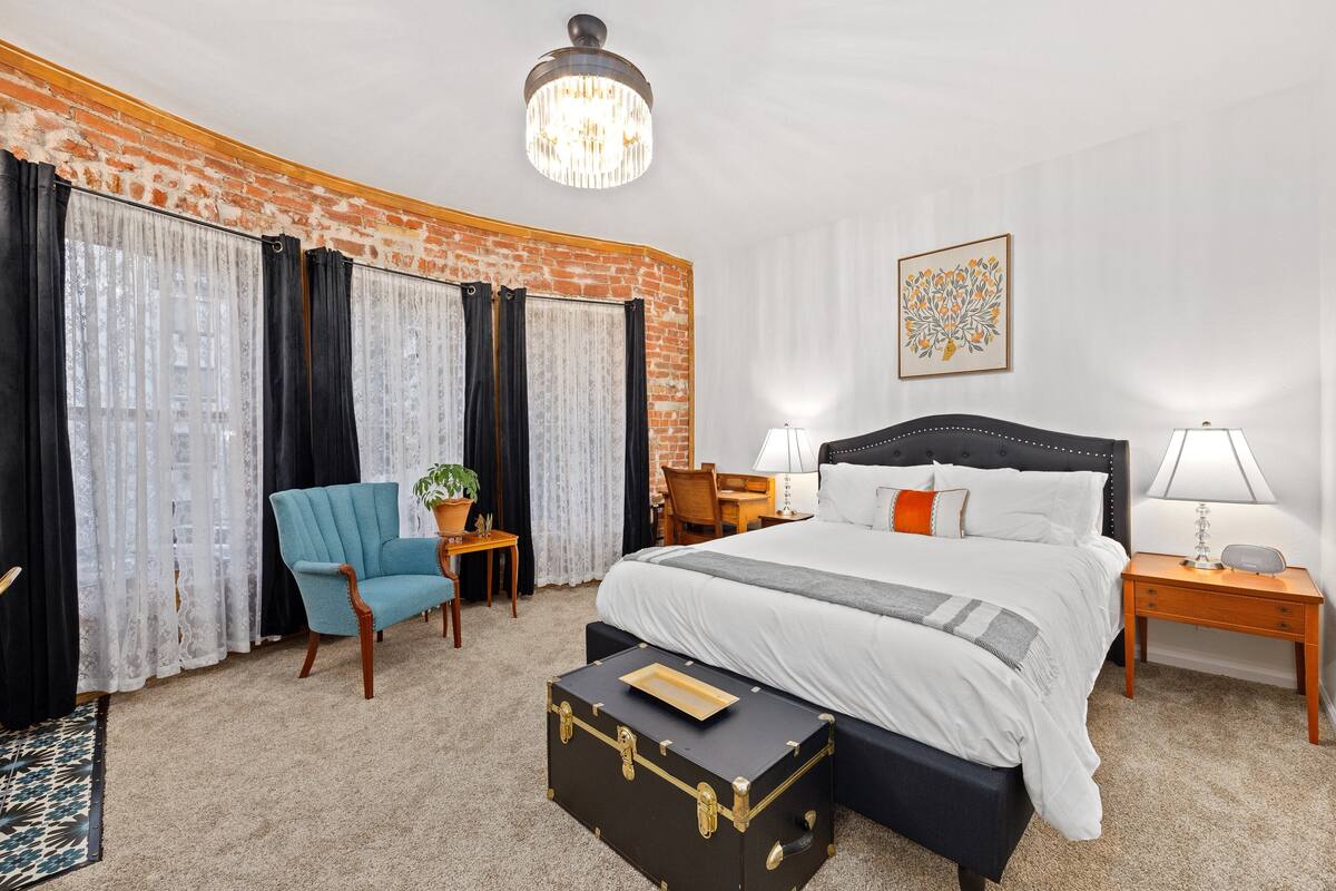 A hotel room with a large bed, a chest of drawers, a desk, a chair, and a suitcase.