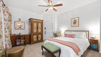 A bedroom with a bed, a desk, a chair, a cabinet, a ceiling fan, and a bedside table with a lamp.