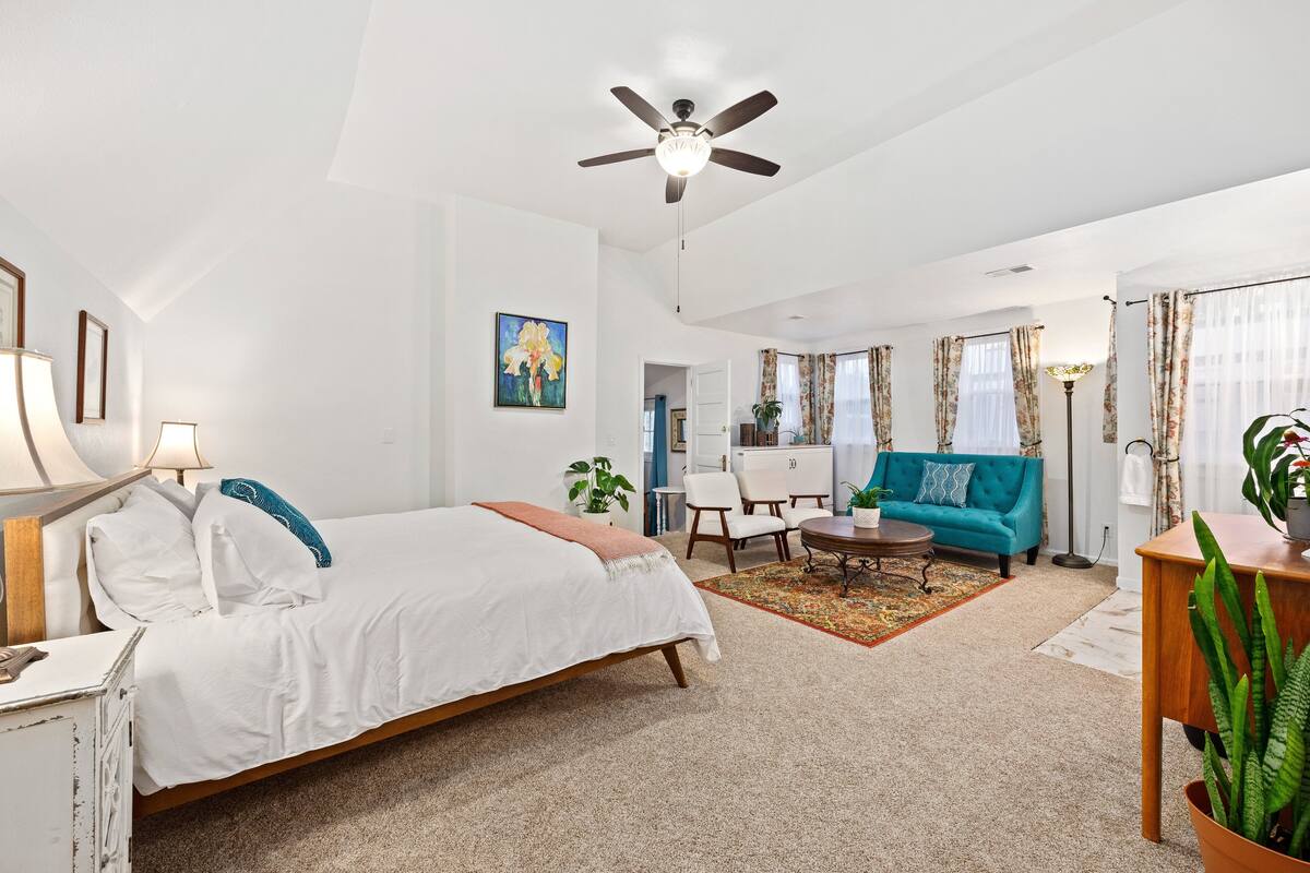 A spacious living room with a large bed, a teal sofa, and a ceiling fan.