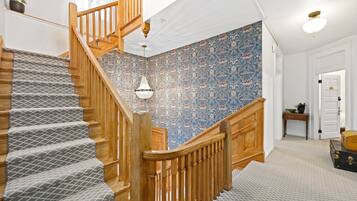 A staircase with a patterned carpet, wooden railing, and a floral wallpapered wall.