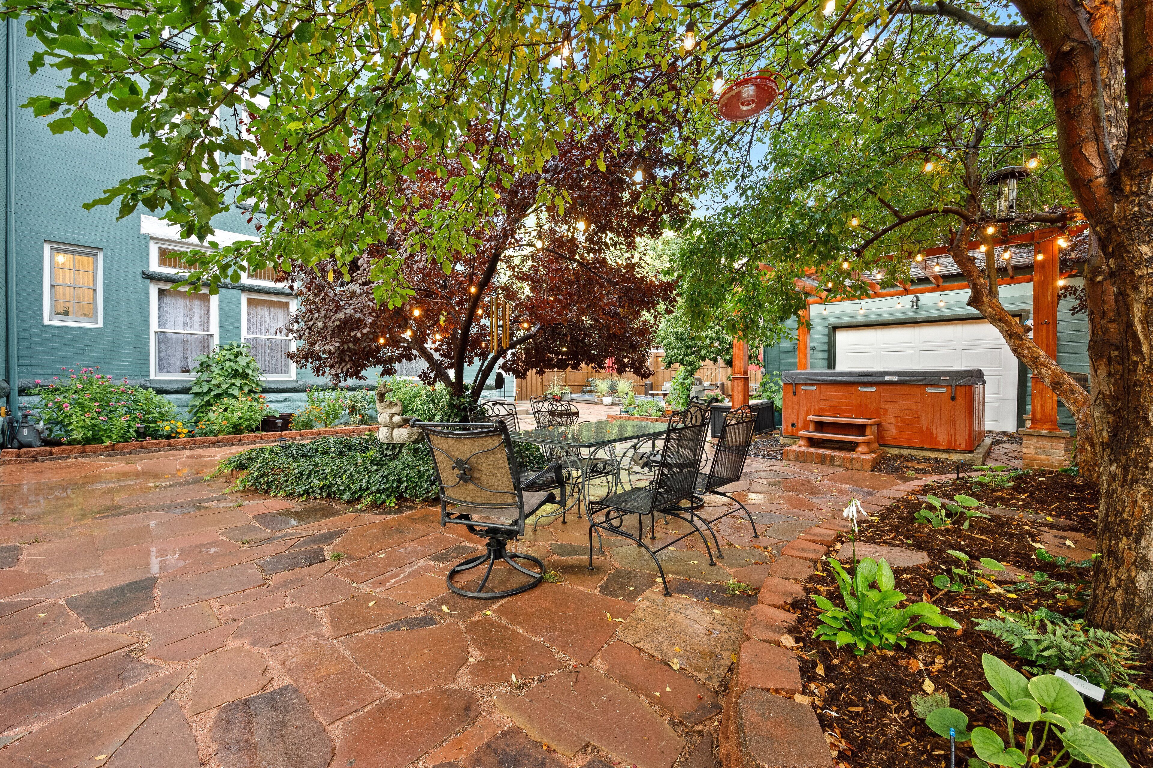 Un patio con suelo de piedra, mobiliario exterior y un árbol que da sombra.