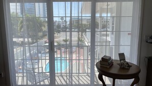 A room with a large window overlooking a pool and buildings. There's a table with books and a decorative item.