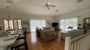 A spacious living area with a dining table, sofas, and a ceiling fan.