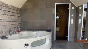 A spa bathroom with a large bathtub, a shower area, and a wooden door. - Fantastic view and magical sunsets! (Algutsrum)