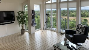 A spacious living room with wooden floors, a mounted TV, a large window with a view of greenery, and a telescope. - Fantastic view and magical sunsets! (Algutsrum)