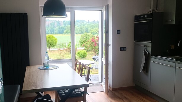 A kitchen with a dining table, chairs, a refrigerator, and a view of a garden through a glass door. - 2 Bedroom Condo in Niederwiesa (Niederwiesa)