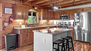 A modern kitchen with wooden cabinets, stainless steel appliances, and a granite countertop. - MODERN UPSCALE CABIN WITH UNOBSTRUCTED LAKE & MOUNTAIN VIEWS (Baxter)