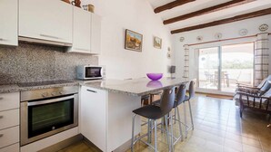 A compact kitchen with a microwave, oven, and bar stools. - Casa Tossa – Pool, Parking & Terrace (27) (Tossa De Mar)