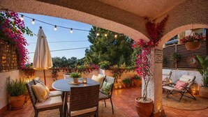 An outdoor patio with a round table, wicker chairs, potted plants, string lights, and a view of the surrounding area. - Casa Tossa – Pool, Parking & Terrace (27) (Tossa De Mar)