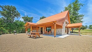 Una cabaña con fachada de piedra, terraza de madera y zona de picnic cubierta.