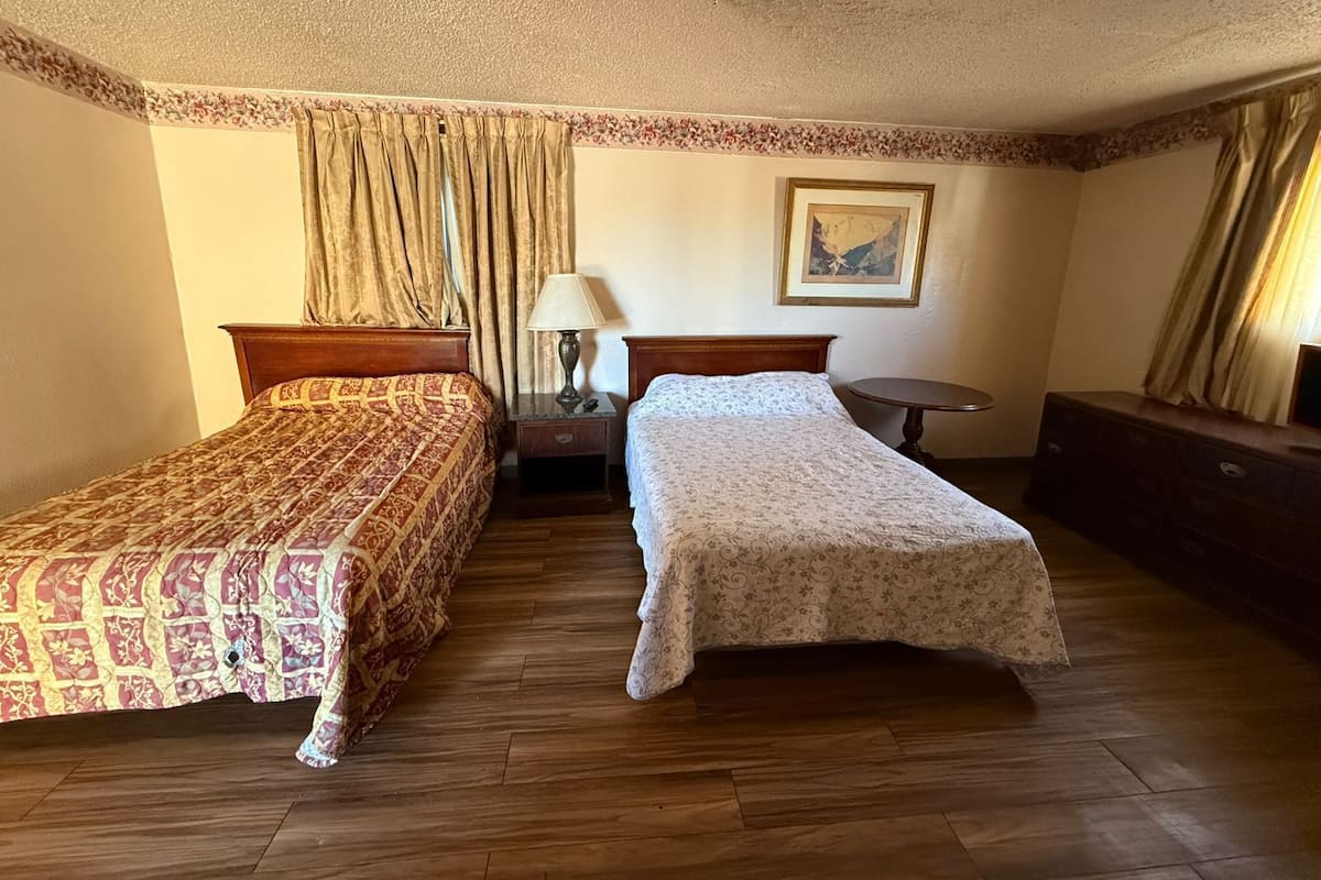 A hotel room with two beds, a nightstand, a lamp, a small round table, and a dresser.