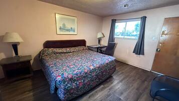 Una habitación pequeña y ordenada con una cama, un escritorio, una silla, una ventana con cortinas y una puerta.
