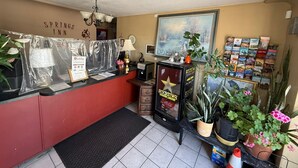 A reception area with a red counter, a framed painting, a Rockstar Energy Drink refrigerator, and a wall-mounted clock. - Springs Inn by Capital O I 25 (Colorado Springs)