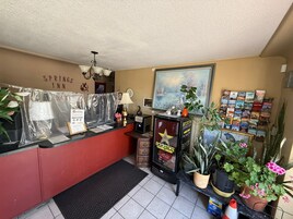 A reception area with a red counter, a framed painting, a Rockstar Energy Drink refrigerator, and a wall-mounted clock.
