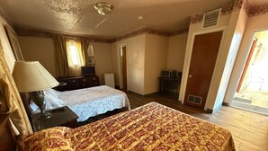 A hotel room with two beds, a desk, a lamp, a TV, and a door leading to a balcony. - Springs Inn by Capital O I 25 (Colorado Springs)