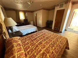 Una habitación de hotel con dos camas, un escritorio, una lámpara, un televisor y una puerta que da a un balcón.