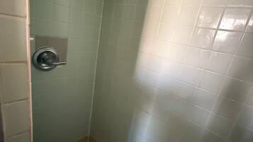 A small, enclosed shower area with tiled walls and floor, a showerhead, and a control panel.
