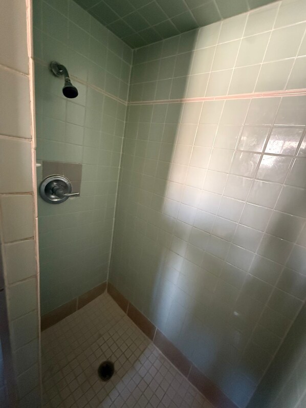 A small, enclosed shower area with tiled walls and floor, a showerhead, and a control panel. - Springs Inn by Capital O I 25 (Colorado Springs)