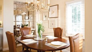 Un comedor con una mesa redonda dispuesta para cuatro personas, rodeada de sillas de cuero. Un candelabro cuelga encima, y hay cuadros enmarcados en la pared.