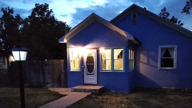 A blue house with a white door and windows, a pathway leading to the entrance, and a wooden fence in the background. - Historic Bluebell. Entire House. 2Br Cozy but spacious (Wheatland)