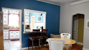 A dining area with a wooden table and chairs, a kitchen visible through an open door, and a blue wall. - Historic Bluebell. Entire House. 2Br Cozy but spacious (Wheatland)