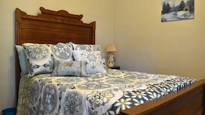A bedroom with a wooden headboard, a patterned bedspread, and a wall-mounted lamp. - Historic Bluebell. Entire House. 2Br Cozy but spacious (Wheatland)